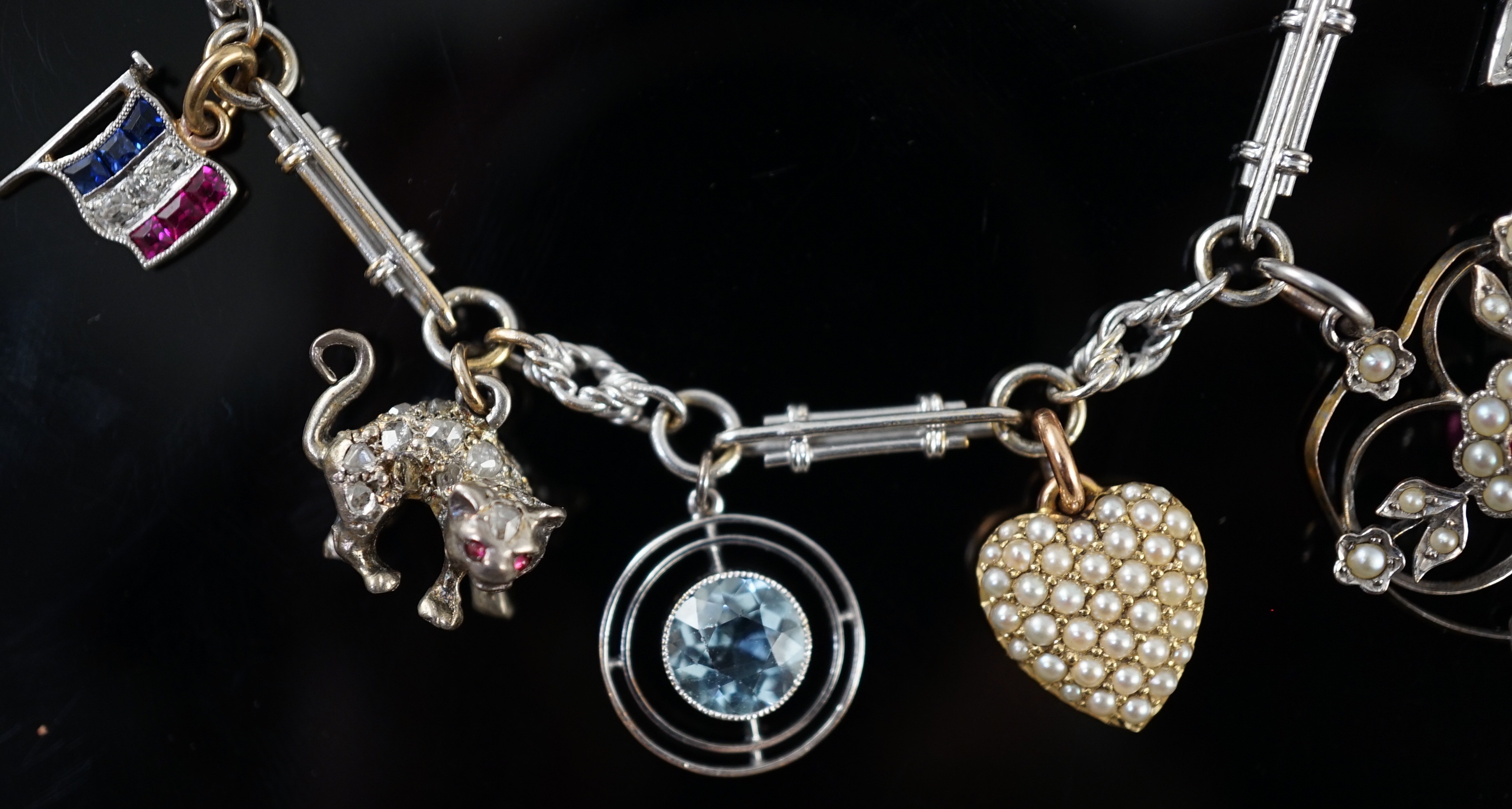 A French 18ct white gold circular and baton link charm bracelet, hung with eleven assorted charms